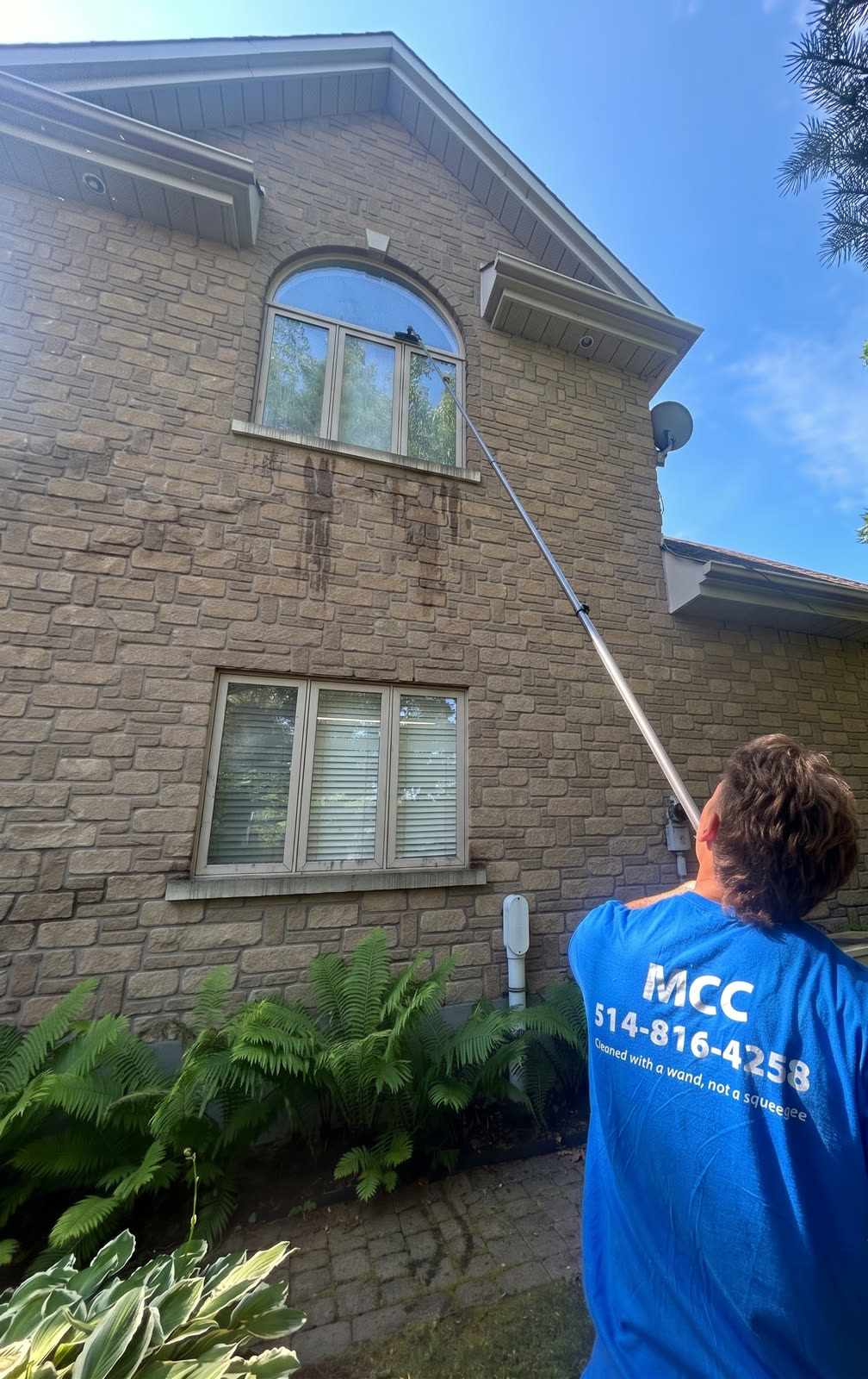 A Magic Cleaning team member cleaning a second storey window with a water fed pole